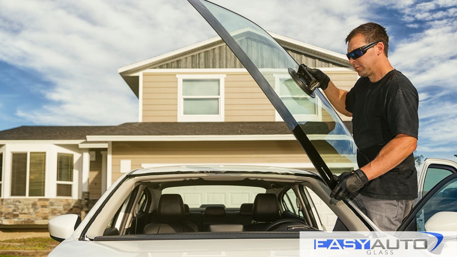 Windshield Replacement of a white car by a man at a suburban home..