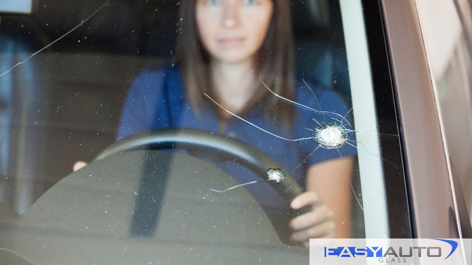 A woman looks out her windshield past the crack that has formed.